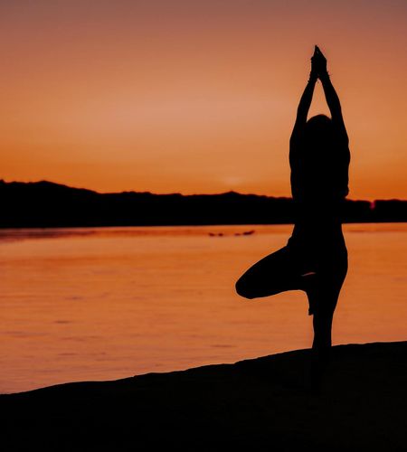Silhouette of a person in a yoga tree pose during sunset.